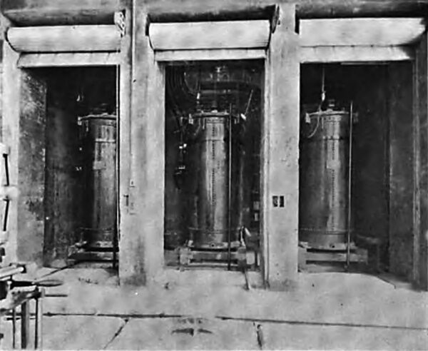 VIEW FROM THE GENERATOR ROOM, SHOWING ONE OF THE THREE GROUPS OF STEP-UP TRANSFORMERS, EACH GROUP CONSISTING OF THREE 2300 - KILOWATT 2300 55,000 -VOLT TRANSFORMERS. EACH GROUP OF THREE TRANSFORMERS IS PLACED IN A CONCRETE CELL WITH CONCRETE AND BRICK VENT THROUGH ROOF, THE ENTRANCE TO THE CELLS BEING PROTECTED WITH IRON ROLLER DOORS.