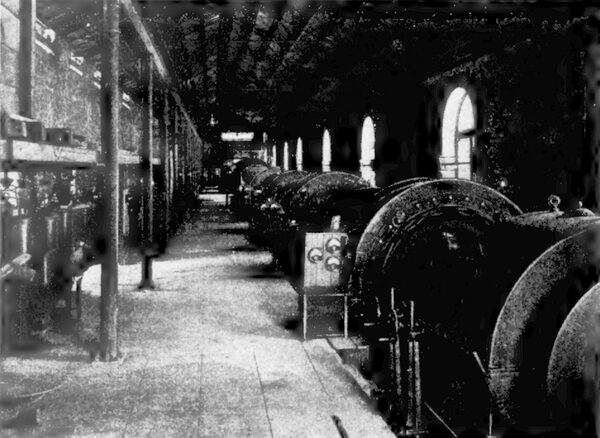 AN INTERIOR VIEW OF THE COLGATE POWER HOUSE, SHOWING ELECTRIC GENERATORS AND TURBINE CASINGS ON THE RIGHT, AND TRANSFORMERS ON THE LEFT.